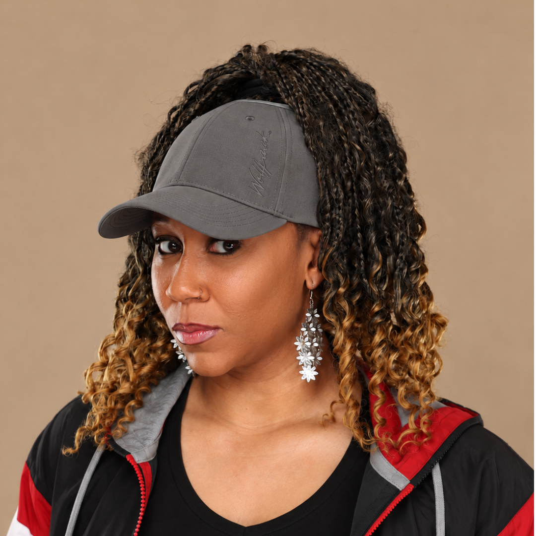 Woman with curly highlighted hair wearing a gray open-top cap against a tan studio background