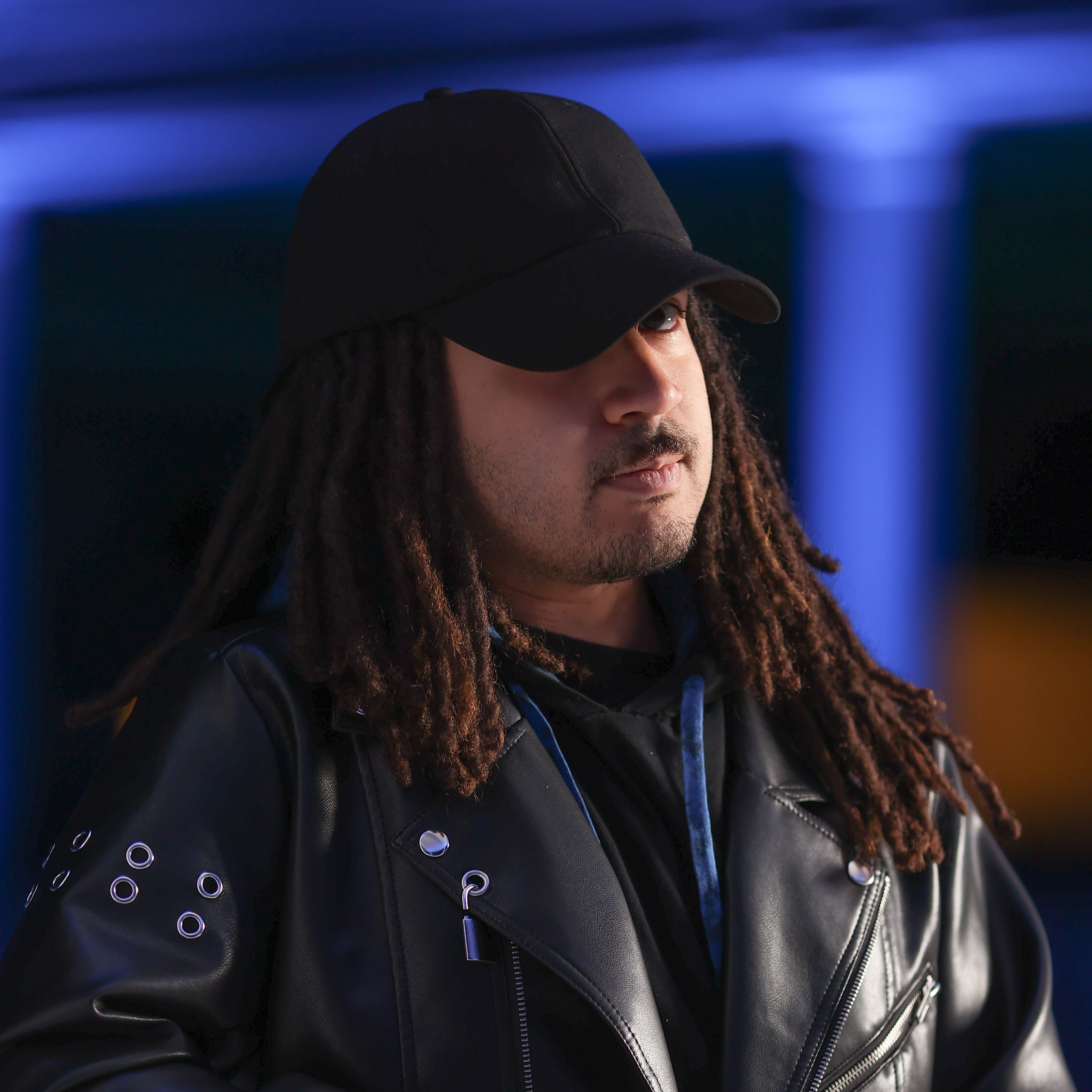 Lifestyle portrait of a model wearing the black Rosebloom HLO with locs, styled with a black leather jacket against a dark blue-lit background.
