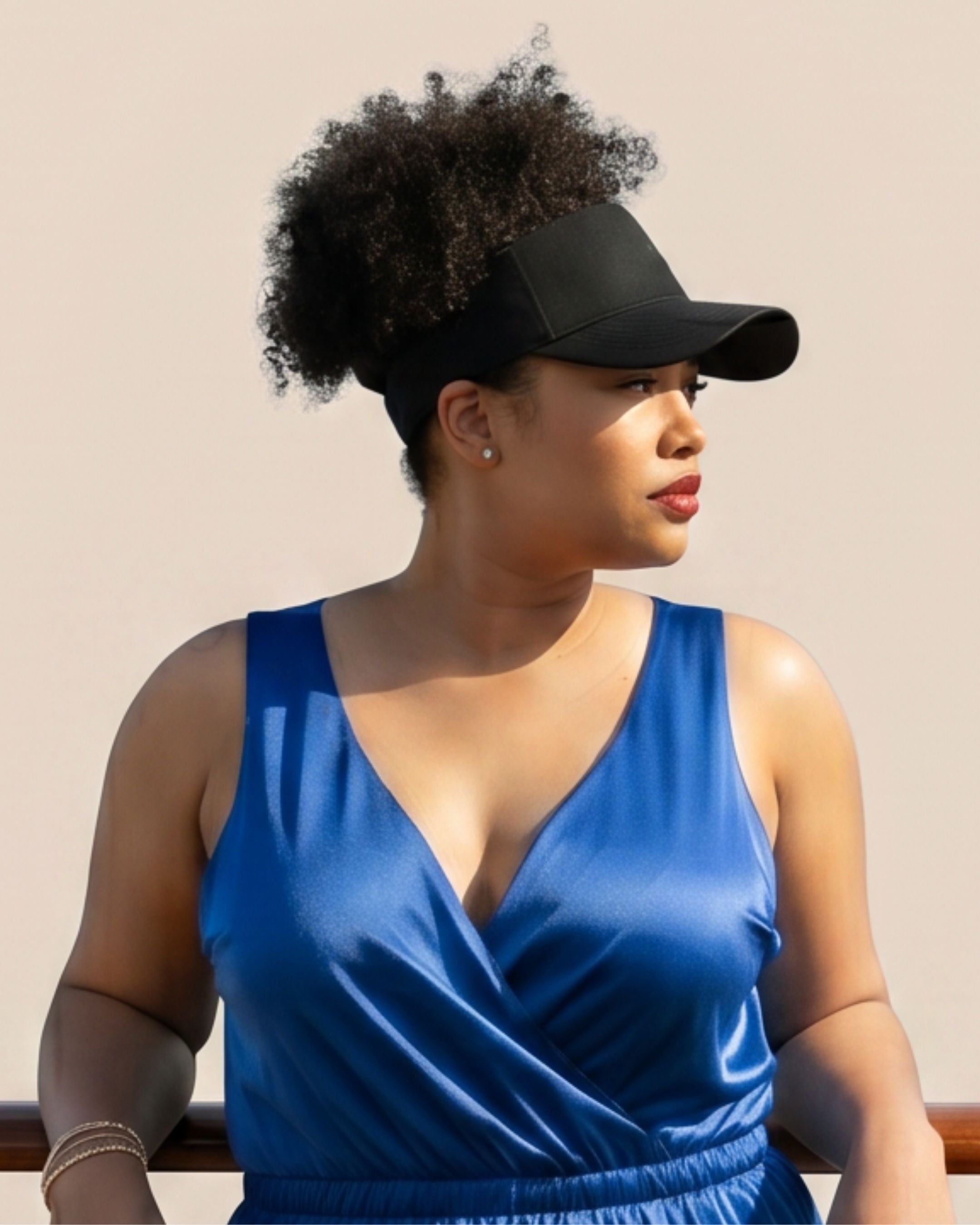 Right profile of a model wearing a black Rosebloom LAZ crown-opening hat with natural hair pulled through the top opening, styled with a blue jumpsuit.