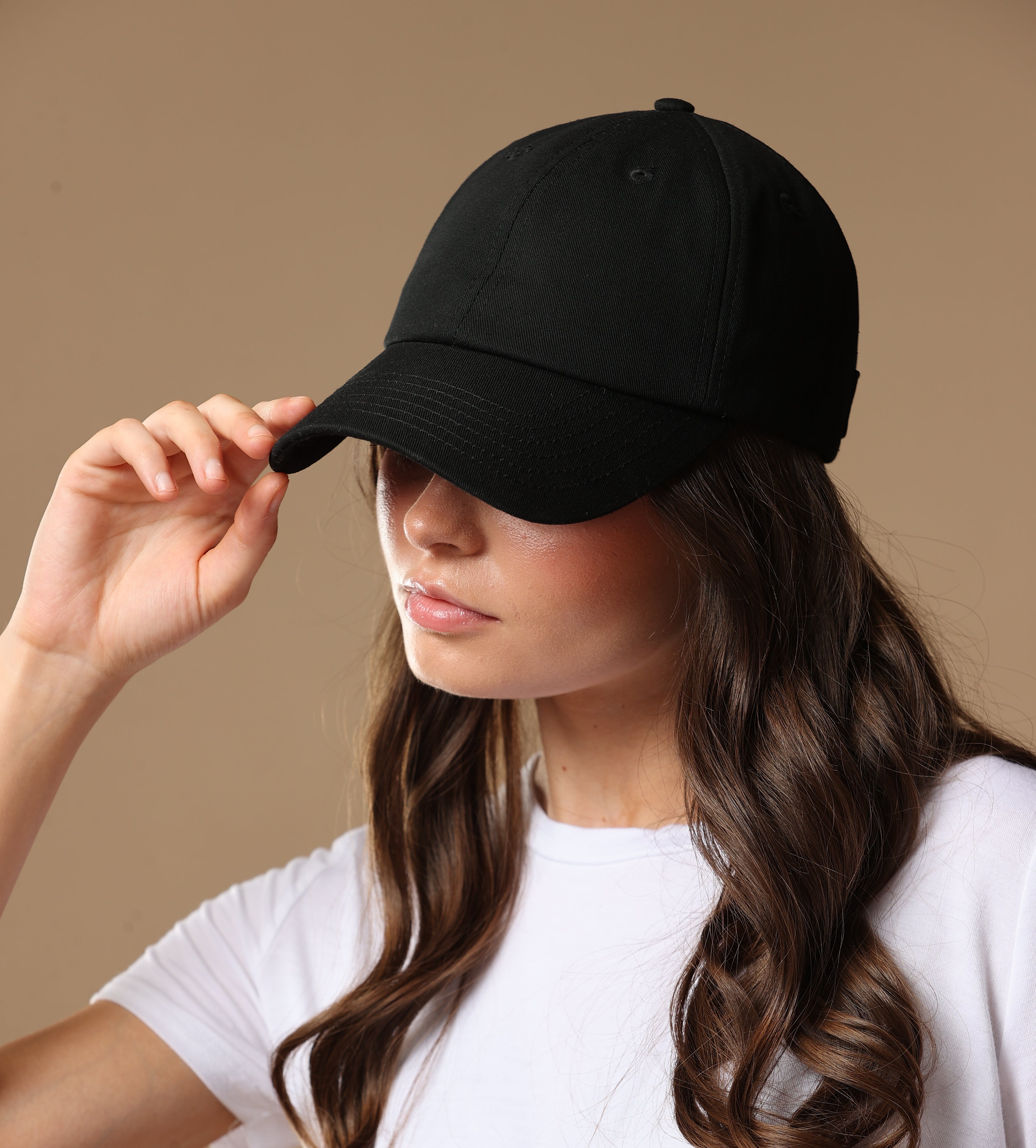 Portrait of a model wearing a black Rosebloom NZR women’s hat, styled with a white top against a beige studio background.