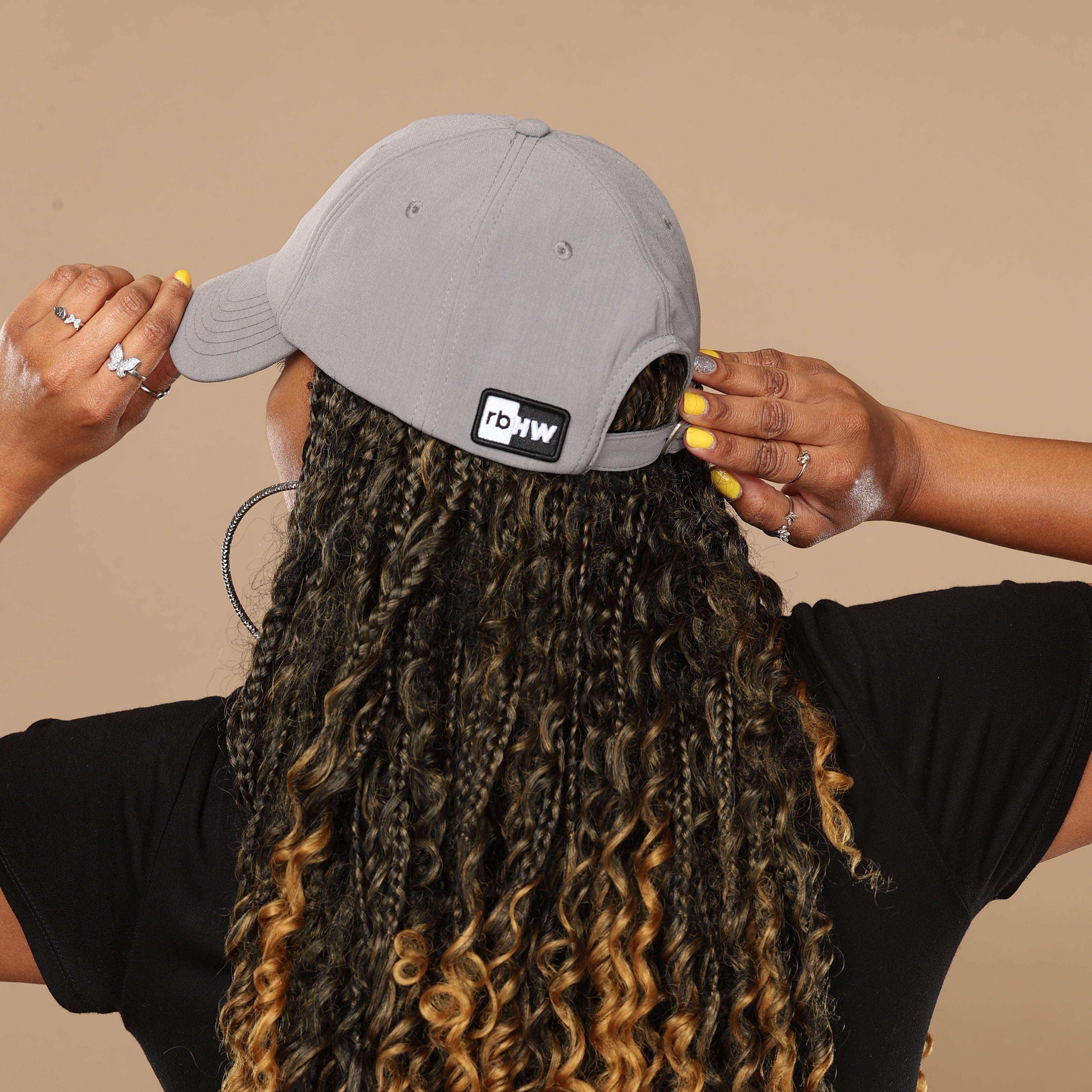 Back view of a model wearing the gray Rosebloom HLO, showing the rear opening, logo patch, and fit over textured hair against a beige studio background.