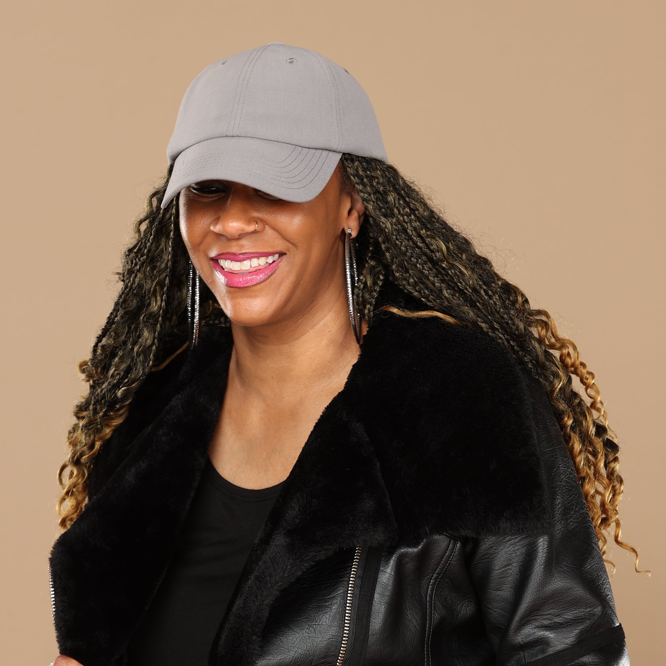 Lifestyle portrait of a model wearing the gray Rosebloom HLO, styled with textured hair, hoop earrings, and a black jacket against a beige studio background.