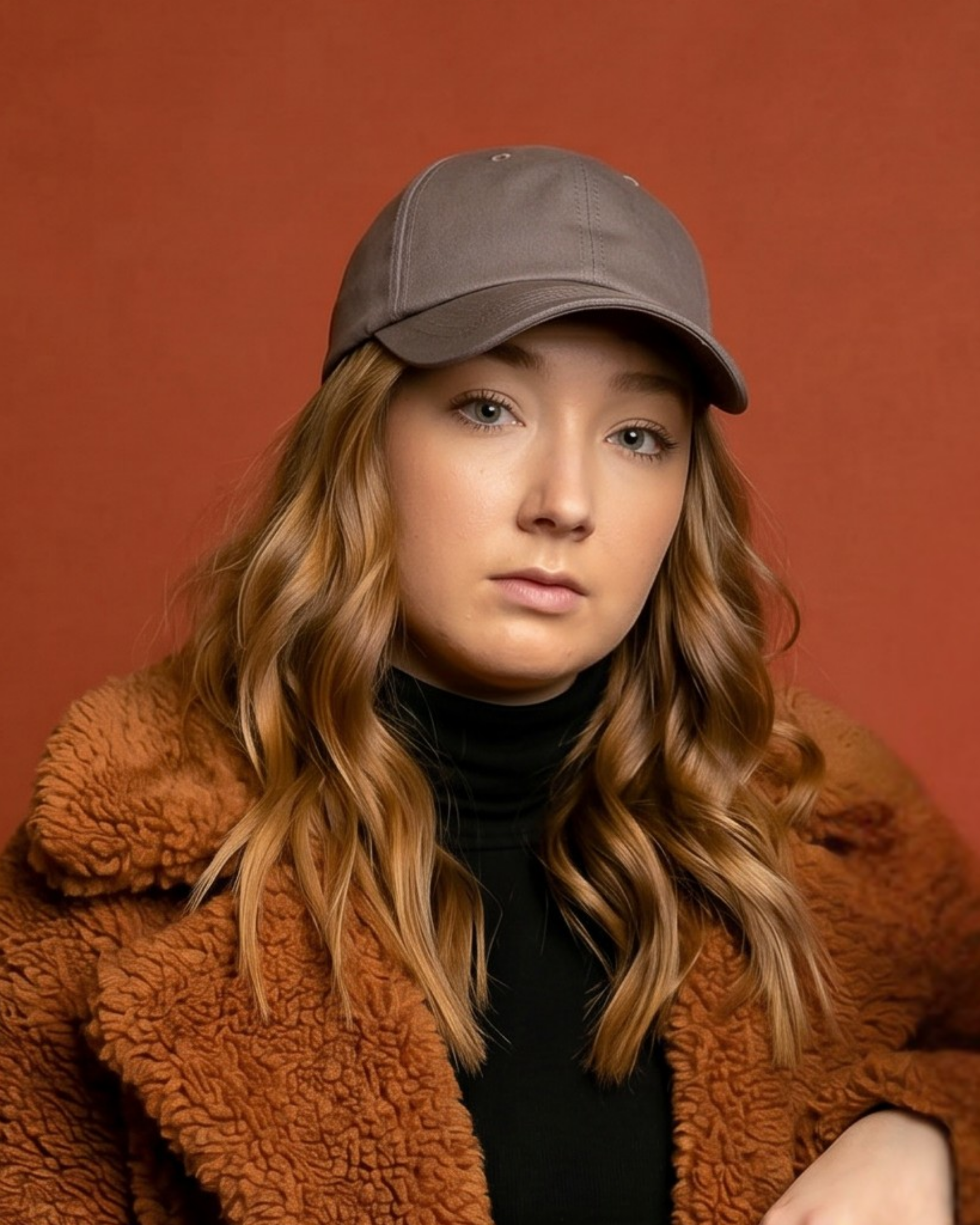 Portrait of a model wearing a gray Rosebloom NZR women’s hat, styled with a black turtleneck and textured brown jacket against a warm studio background.