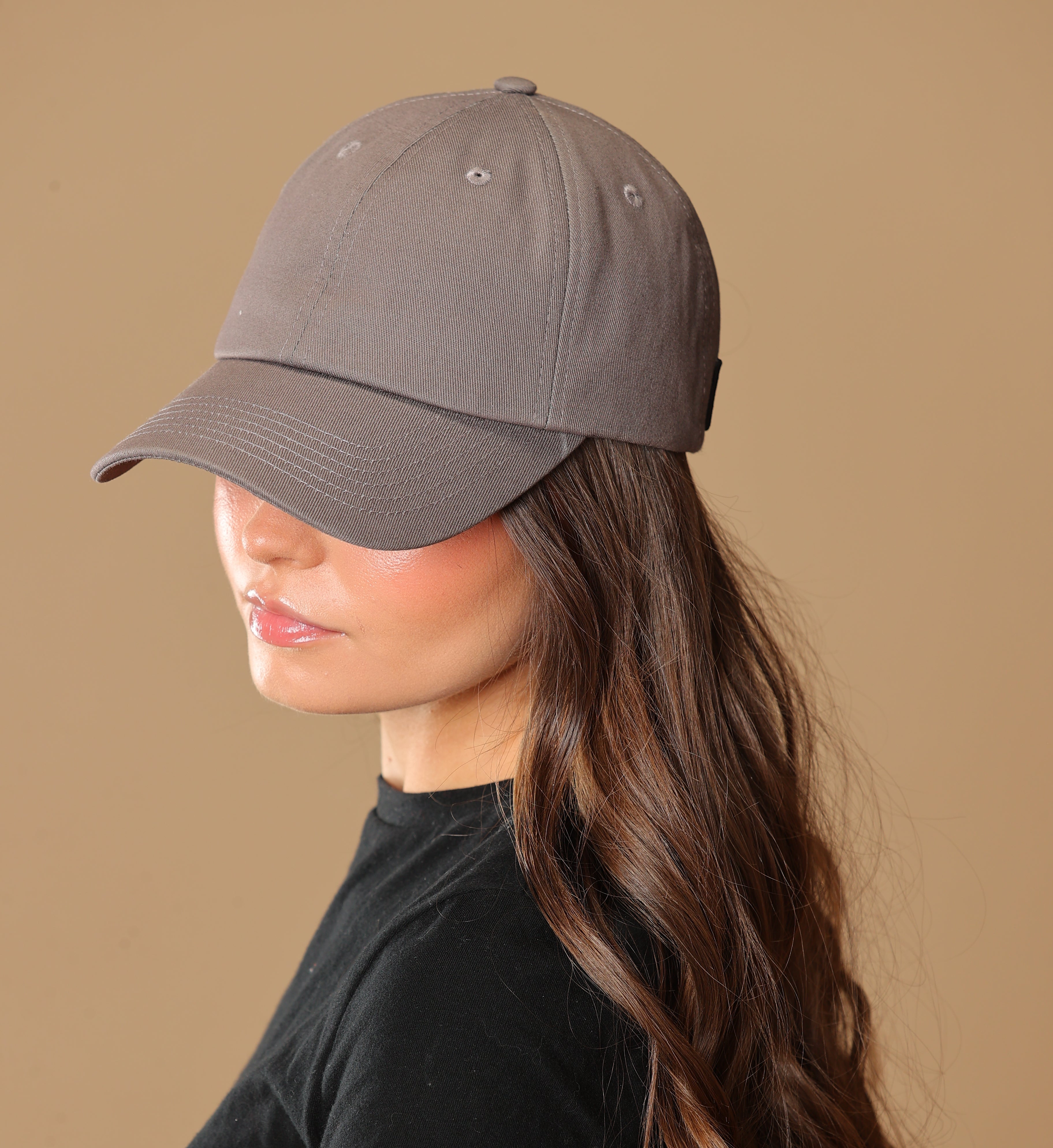 Side portrait of a model wearing a gray Rosebloom NZR women’s hat, styled with a black top against a beige studio background.