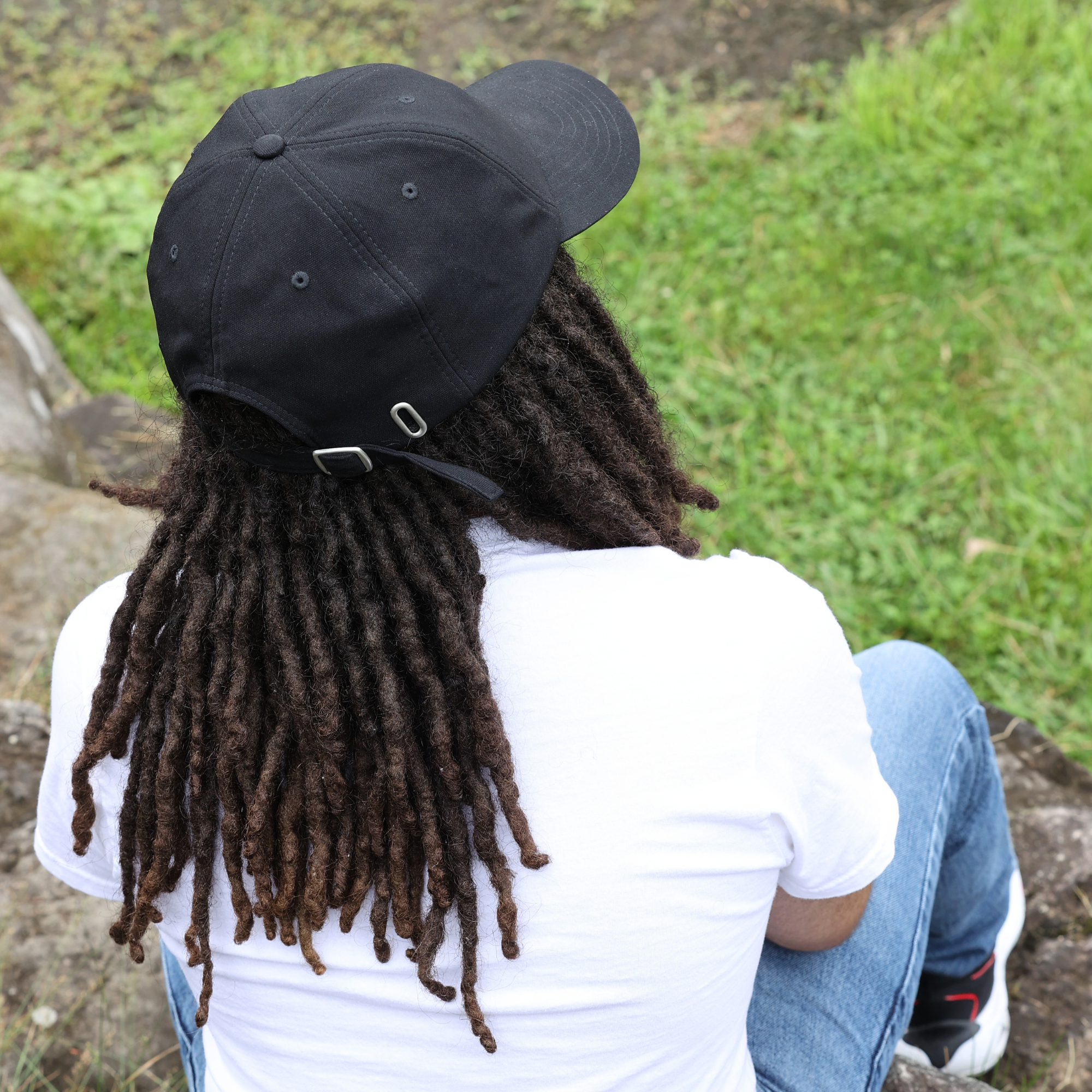 Model shown from behind wearing the black Rosebloom HLO closed crown hat, showing room for locs, textured hair, and protective styles.