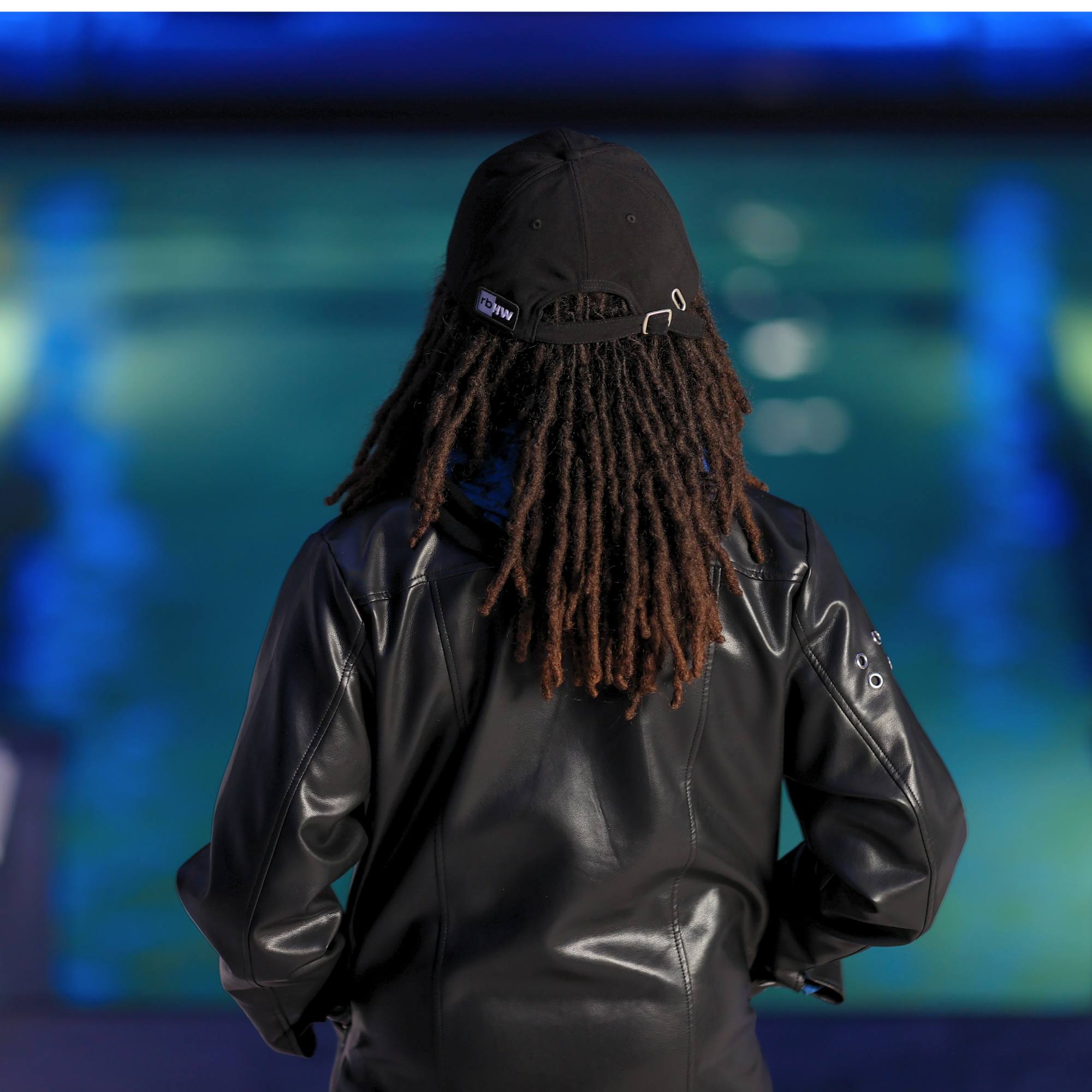 Model shown from behind wearing the black Rosebloom HLO closed crown hat, showing room for locs, textured hair, and protective styles.