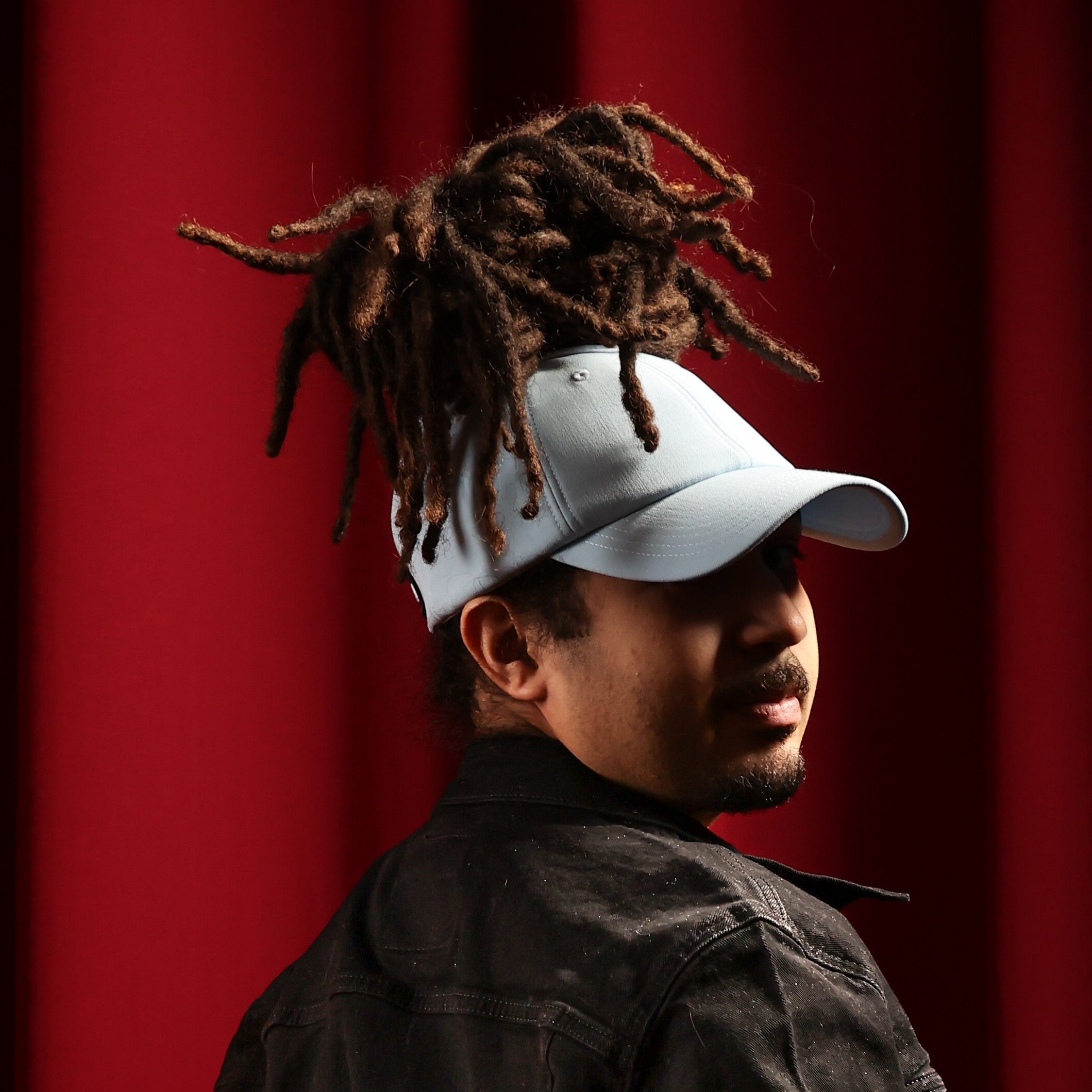Model looking over their shoulder while wearing the baby blue Rosebloom JAX PETAL crown-height opening hat, showing room for locs, textured hair, and protective styles.