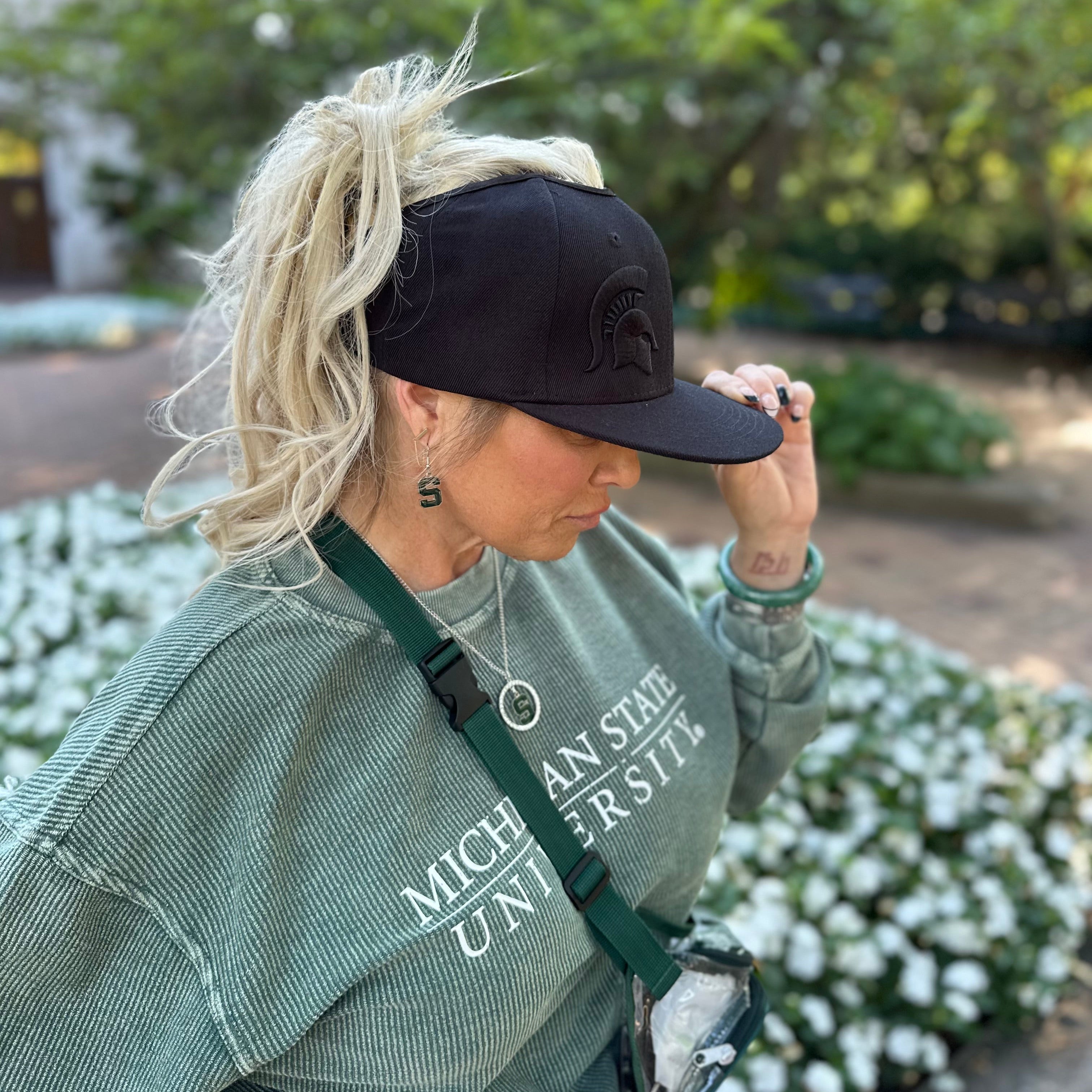 Lifestyle portrait of a model wearing the black Rosebloom Michigan State GZO SNAP with a tonal embroidered Spartan logo, styled with a high ponytail outdoors.