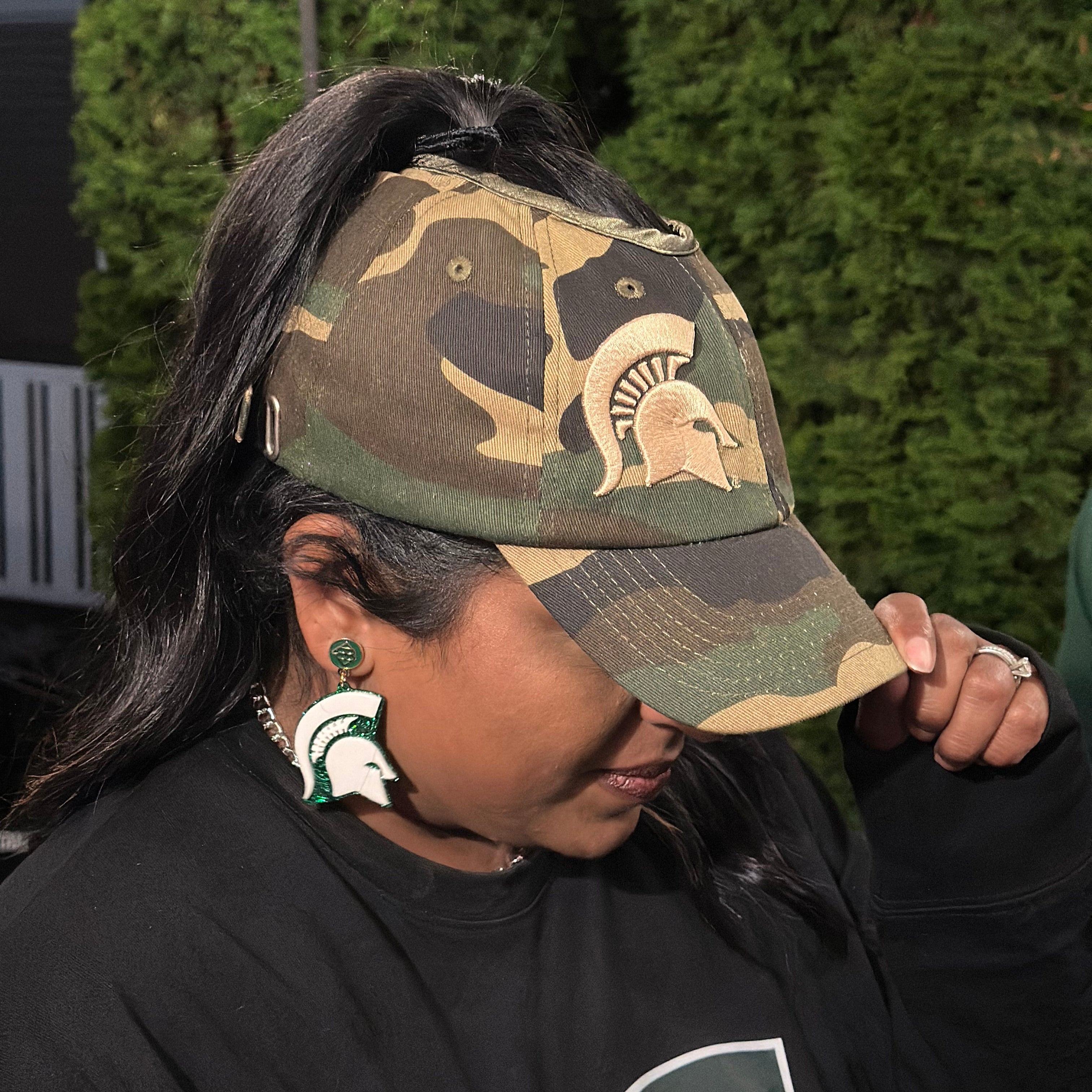 Lifestyle portrait of a fan wearing the camo Rosebloom Michigan State PNT high ponytail hat with an embroidered Spartan logo, styled outdoors in Michigan State apparel.