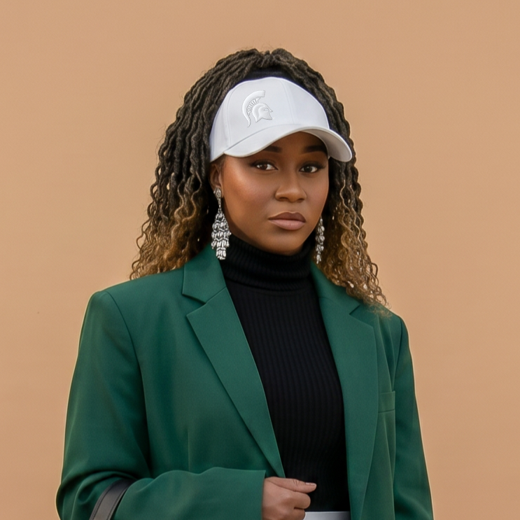 Portrait of a model wearing the white Rosebloom Michigan State LAZ with an embroidered Spartan logo, styled with textured hair through the crown opening and a green blazer against a beige studio background.