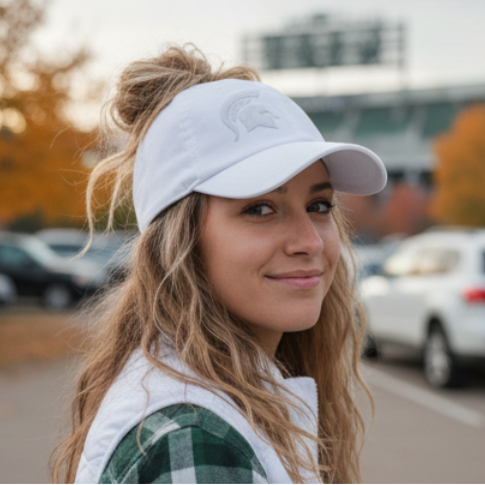 Lifestyle portrait of a model wearing the white Rosebloom Michigan State PNT high ponytail hat with an embroidered Spartan logo, styled outdoors in a parking lot setting.