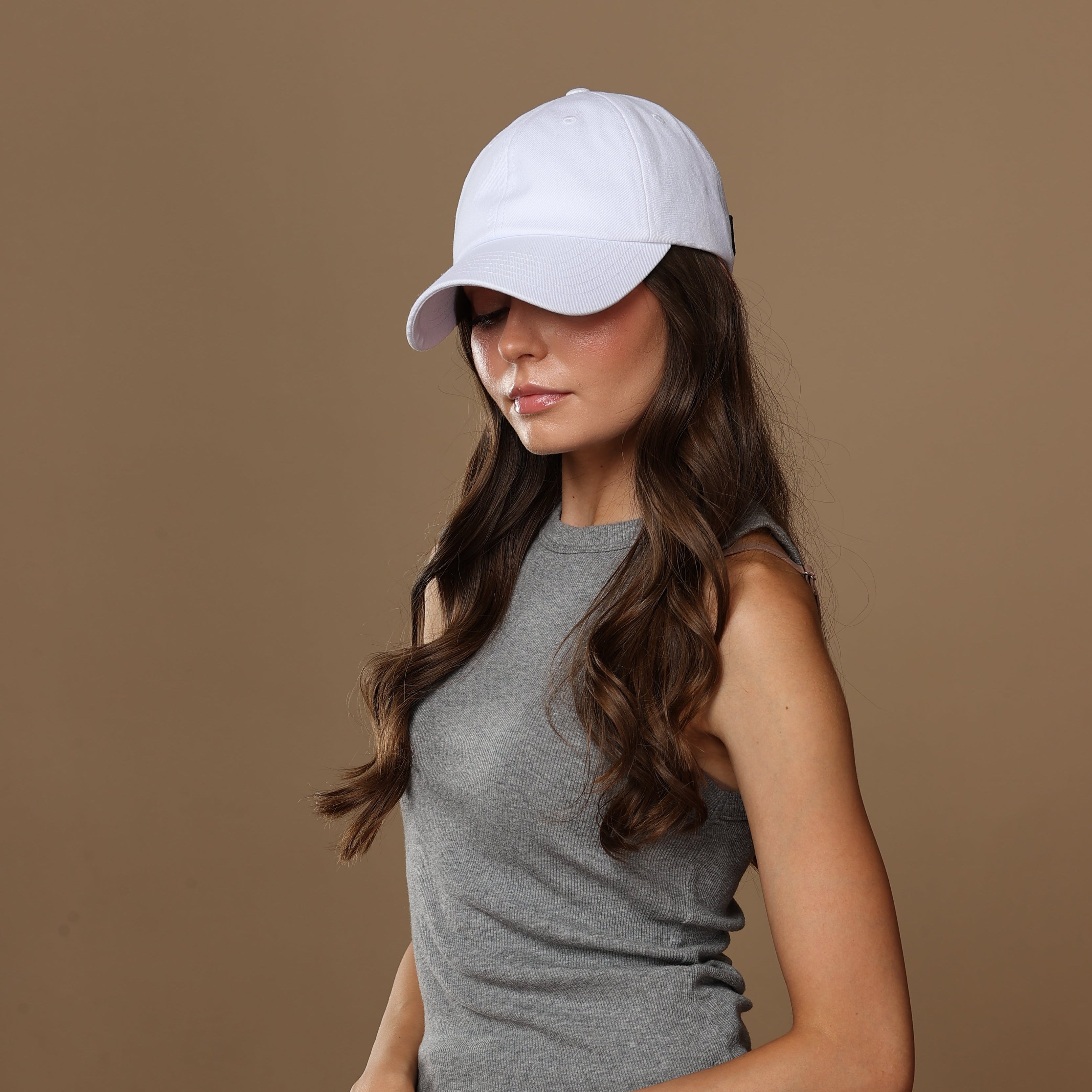 Side portrait of a model wearing a white Rosebloom NZR women’s hat, styled with a gray sleeveless top against a beige studio background.