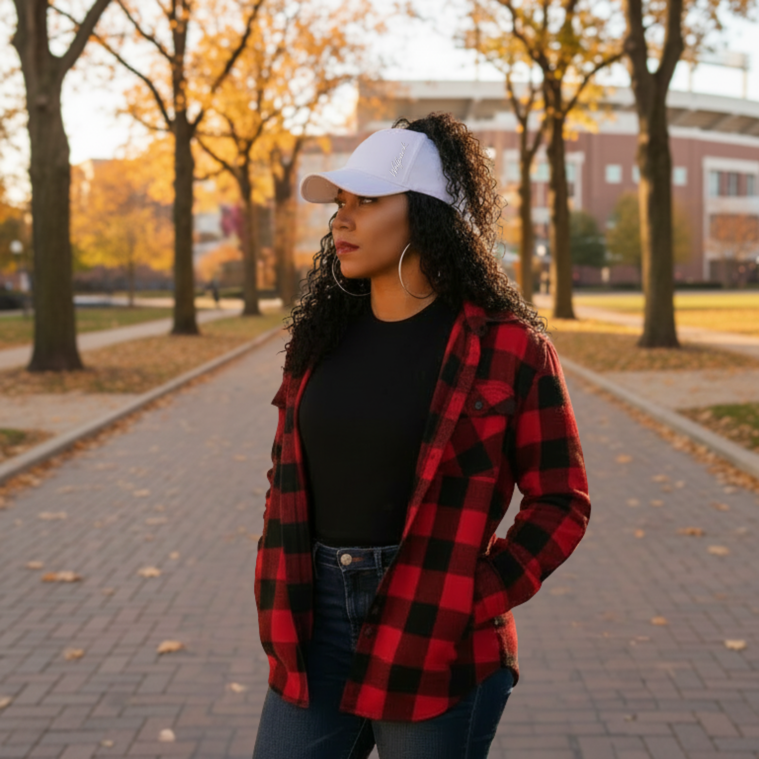 Woman with curly hair wearing a white Rosebloom open-top cap on a tree-lined campus walkway in fall.