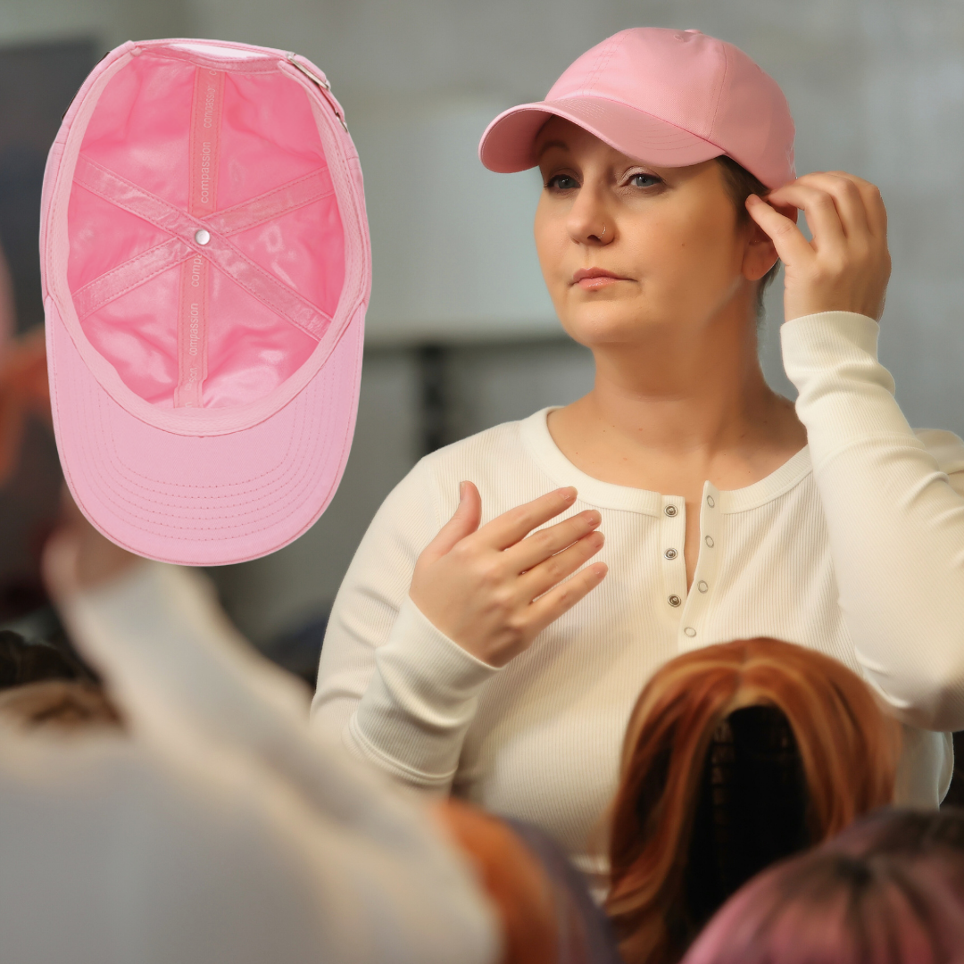 a woman wearing a pink satin lined hat for cancer patients and hair loss examines her reflection in the mirror