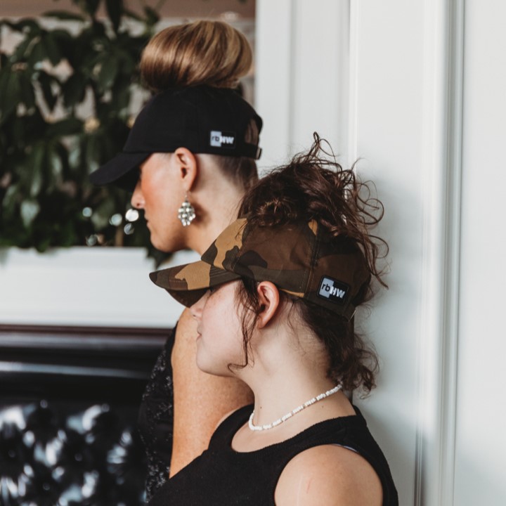 two women stand together wearing satin lined ponytail hats for women