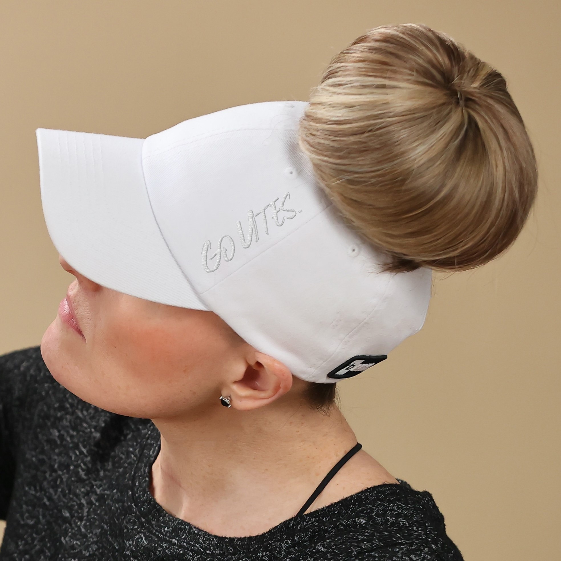 a woman with a high bun wears a satin lined University of Utah ponytail hat for women